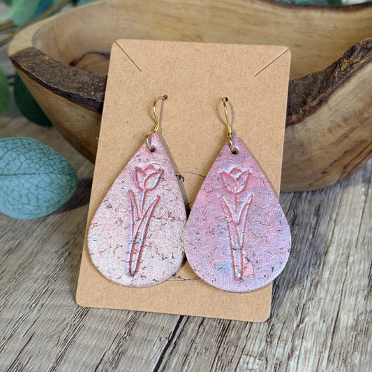 Teardrop-shaped earrings with floral design on a brown card, placed on a wooden surface.