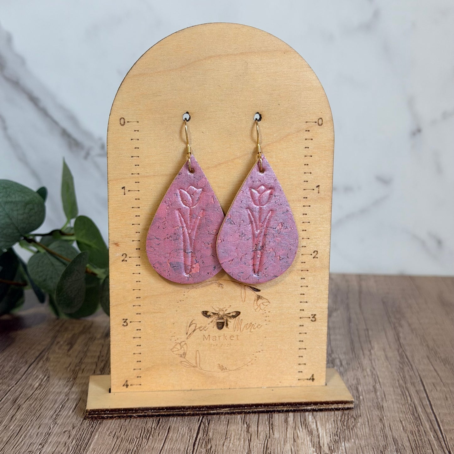 Pink teardrop earrings on a wooden stand with a marble background
