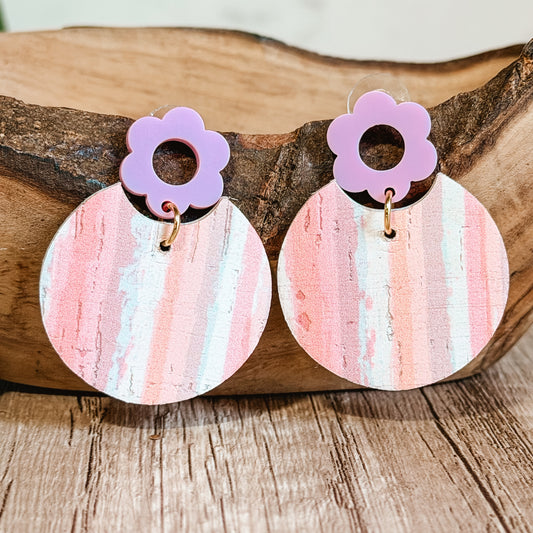 Pair of earrings with pink and purple floral tops and striped circular bases on a wooden surface.