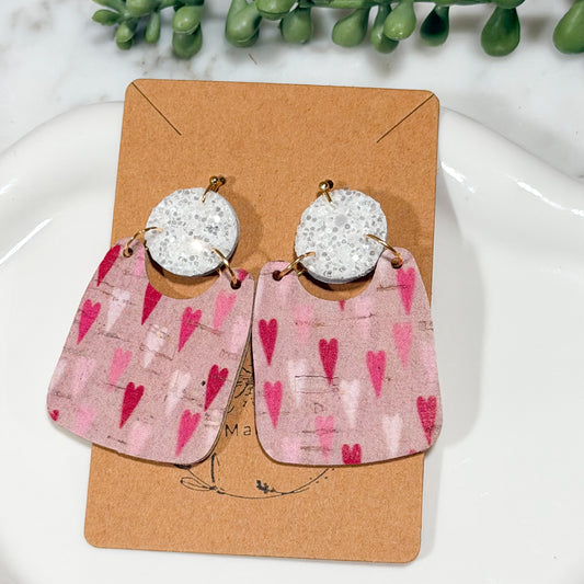 Earrings with pink heart pattern on a display card with greenery in the background