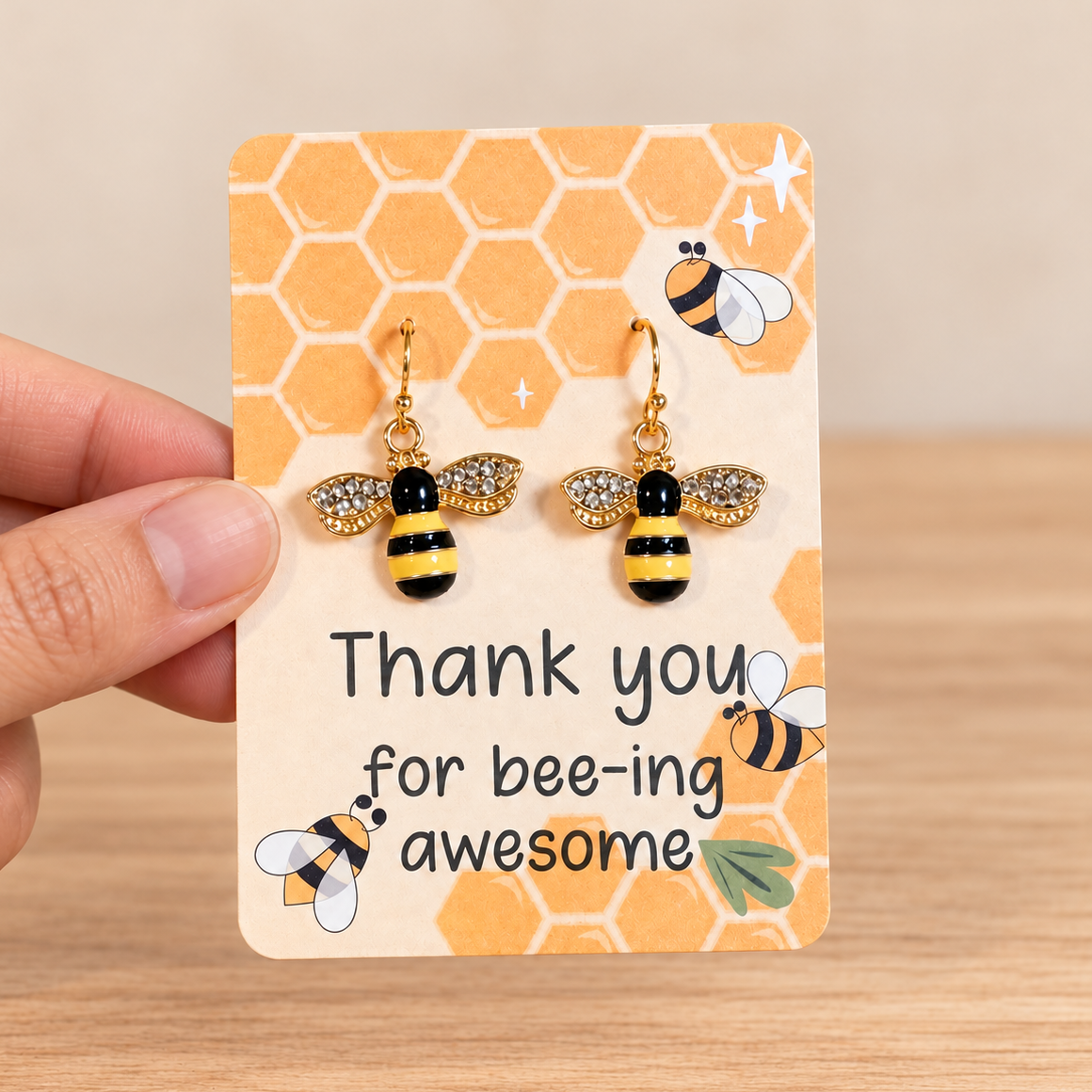 Natural hand holding sparkling black and yellow bee earrings against a simple neutral background