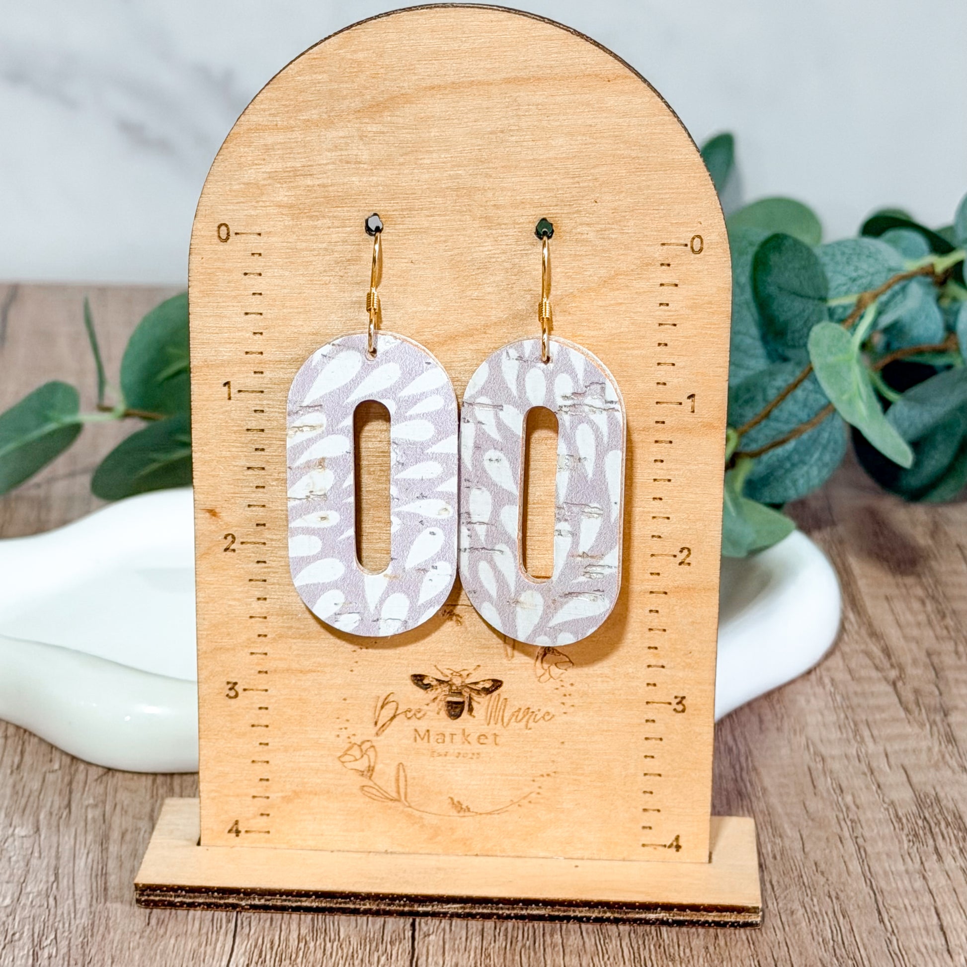 Light lavender petal cutout earrings hanging on a wooden Bee Marie Market earring size stand.