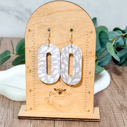 Light lavender petal cutout earrings hanging on a wooden Bee Marie Market earring size stand.