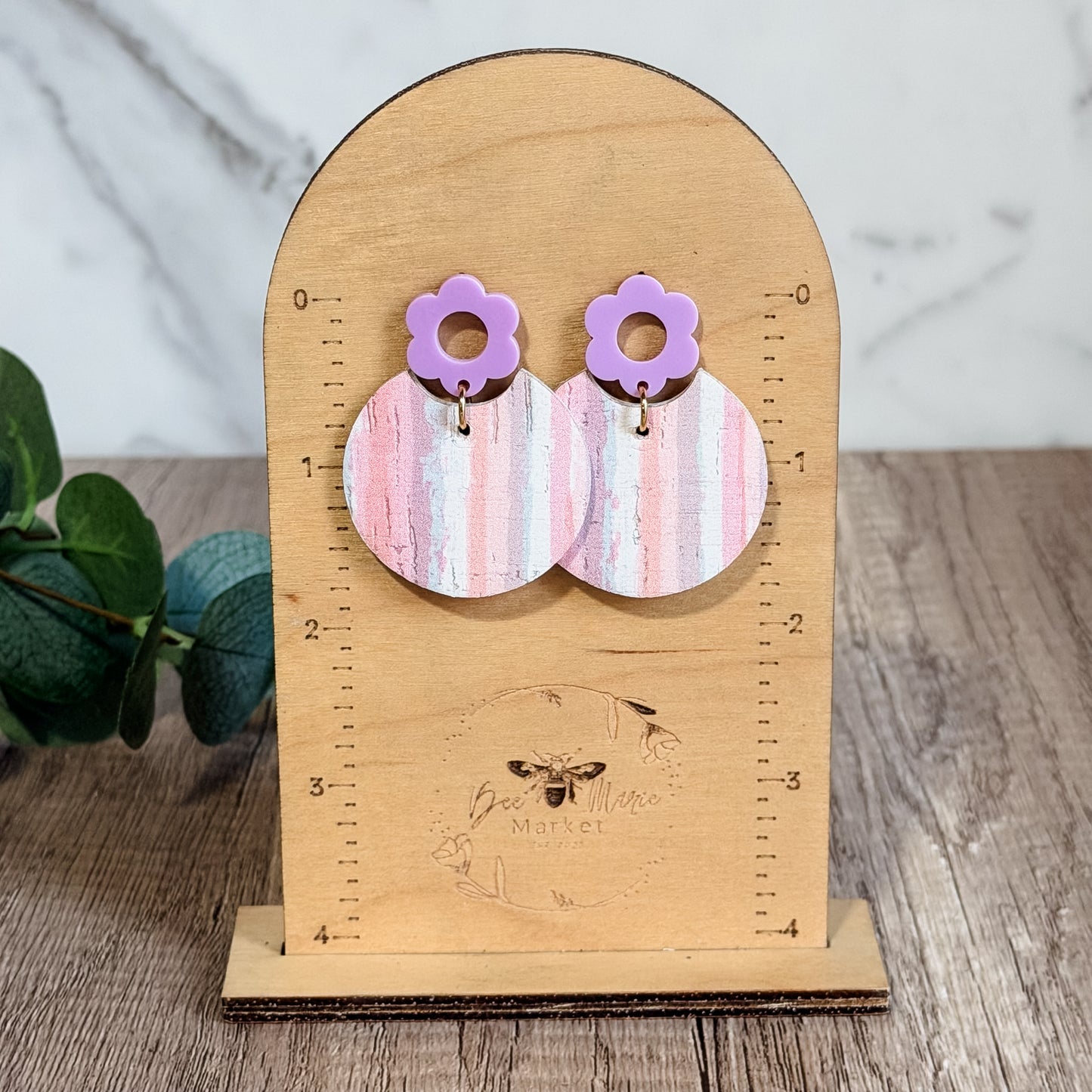 Pair of earrings on a wooden stand with a plant in the background