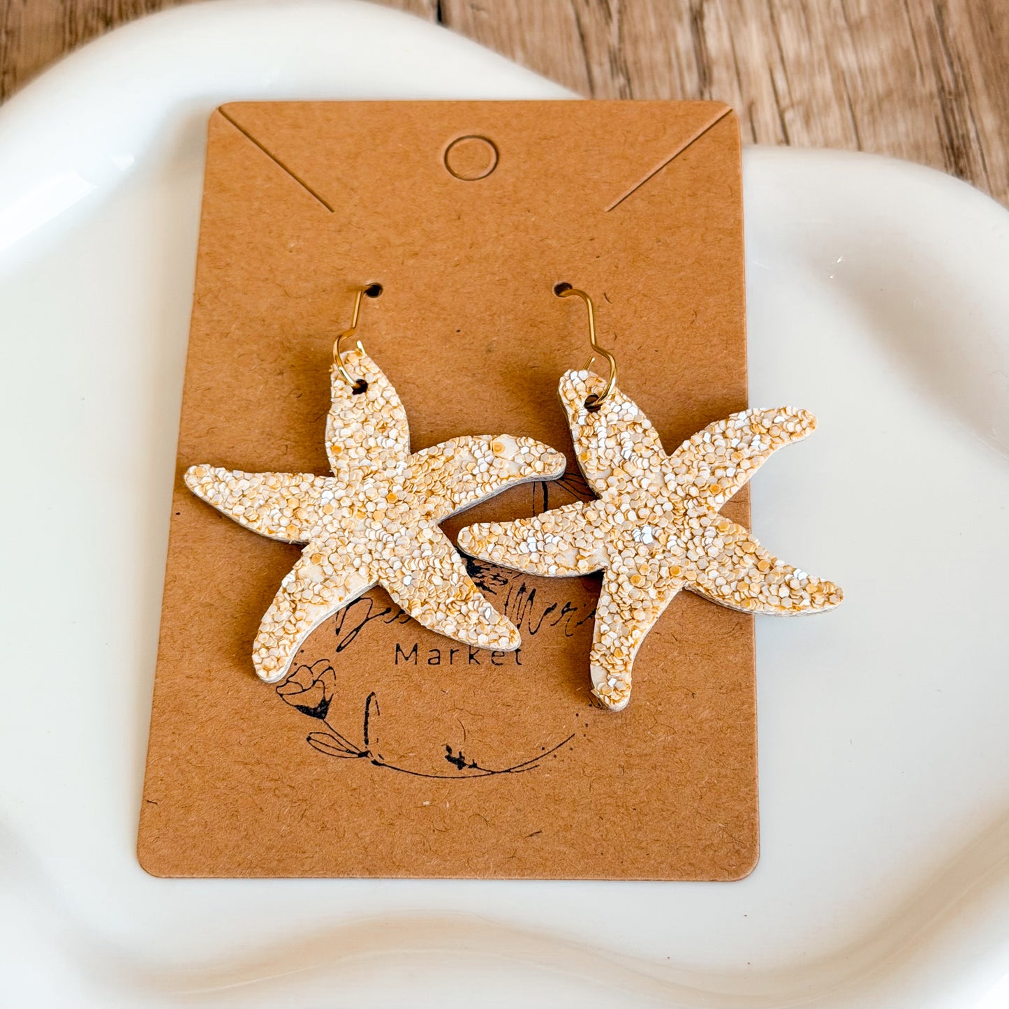 Lightweight handmade starfish earrings with textured neutral finish and gold hypoallergenic hooks displayed on wood and neutral backgrounds.