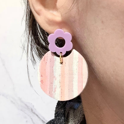 Earring with a pink circular design and purple flower-shaped top worn by a person.