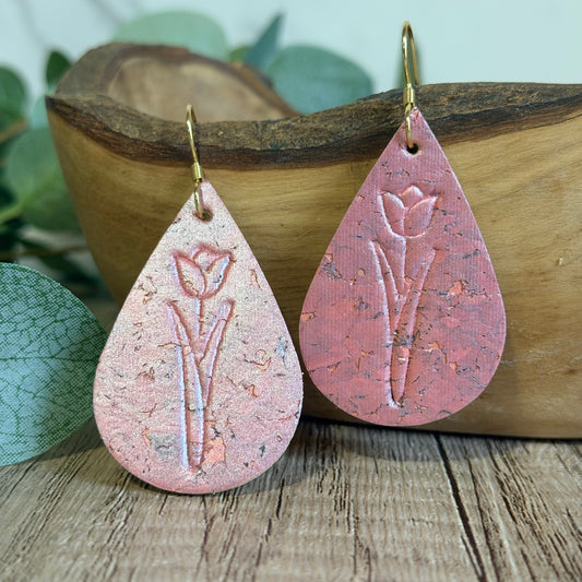 Teardrop-shaped pink earrings with floral design on a wooden surface