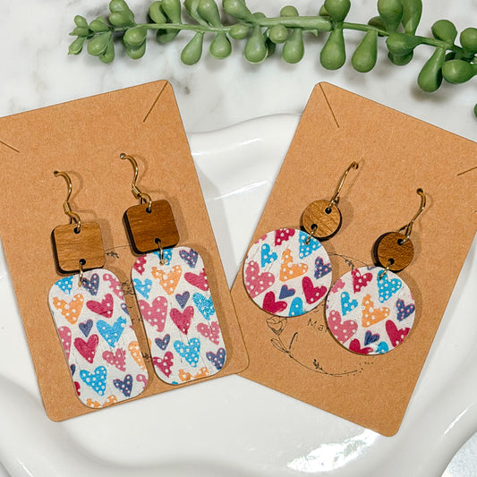 Colorful heart-patterned earrings on brown card with green leaves in the background