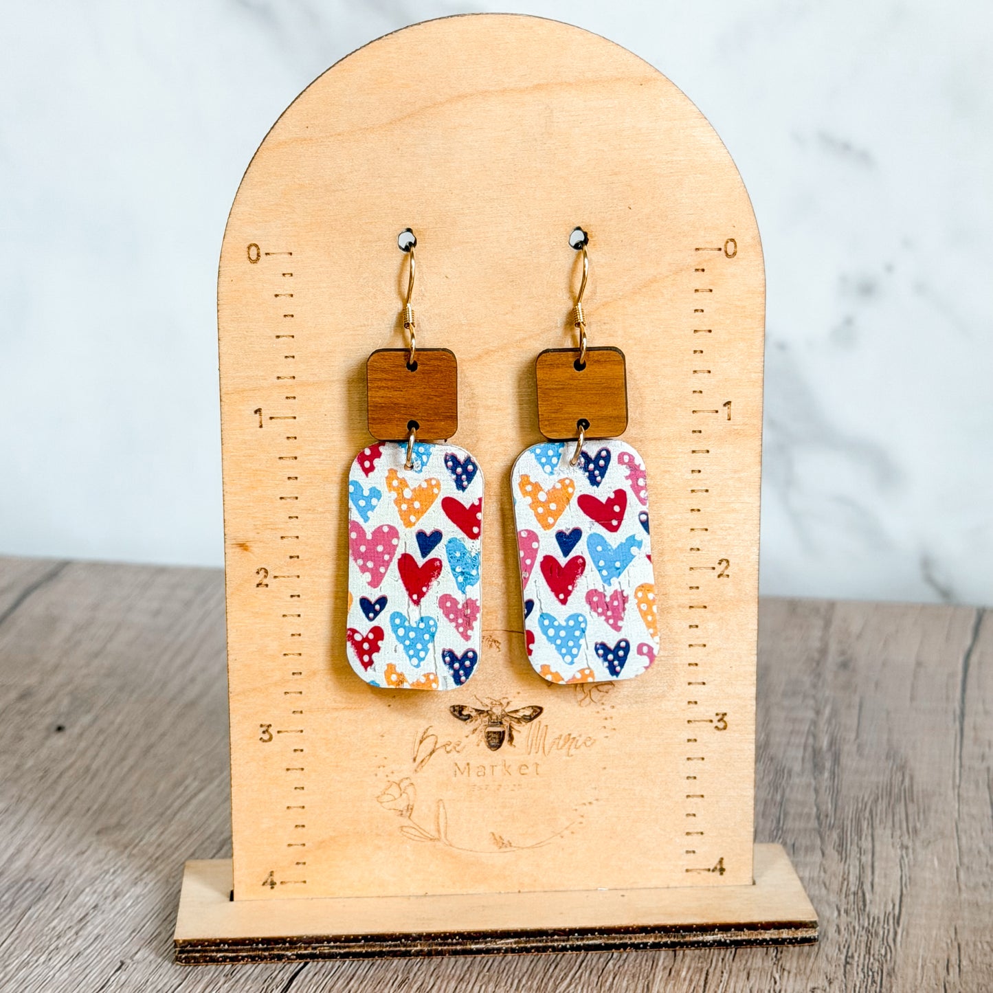 Pair of earrings with heart and polka dot design on a wooden stand.