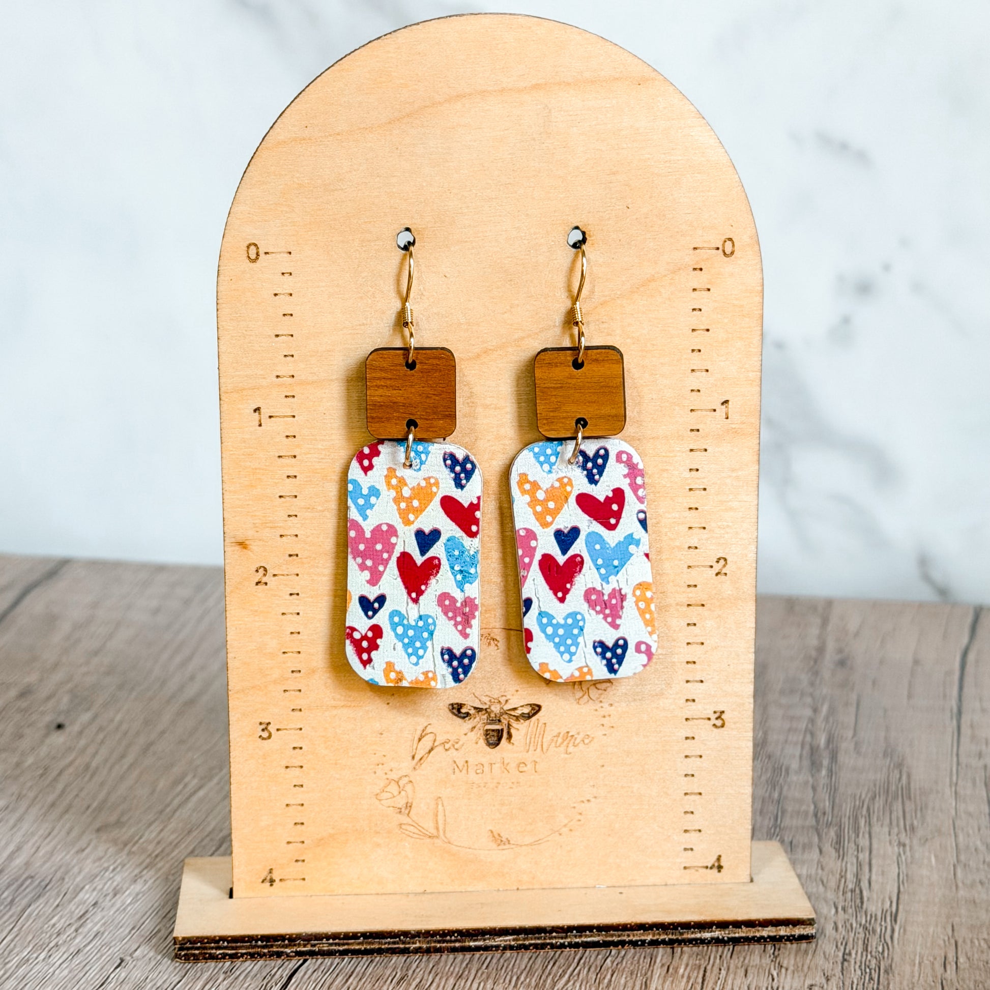 Pair of earrings with heart and polka dot design on a wooden stand.