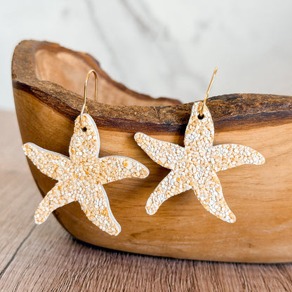 Lightweight handmade starfish earrings with textured neutral finish and gold hypoallergenic hooks displayed on wood and neutral backgrounds.