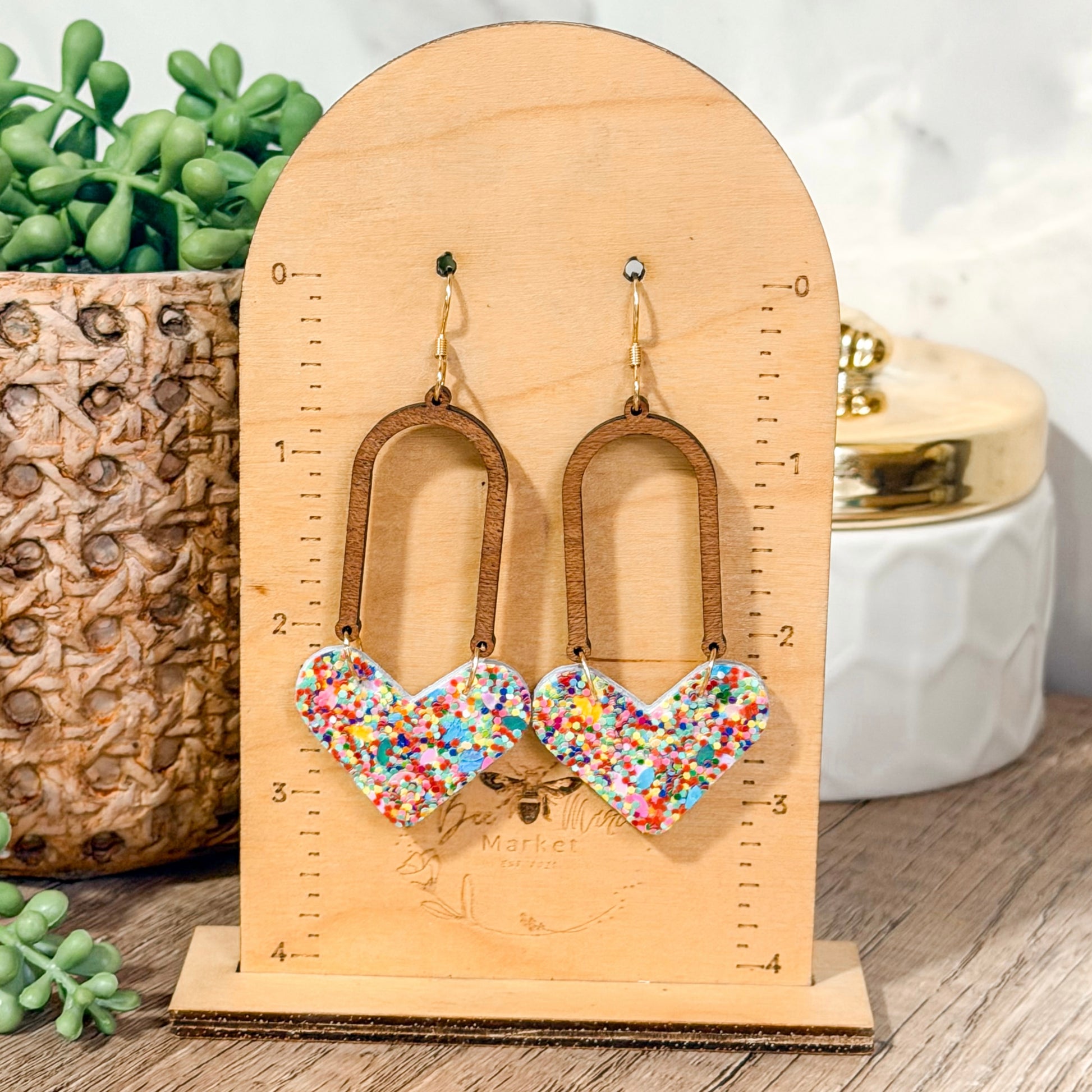 Colorful heart-shaped earrings on a wooden stand with plants and decor in the background