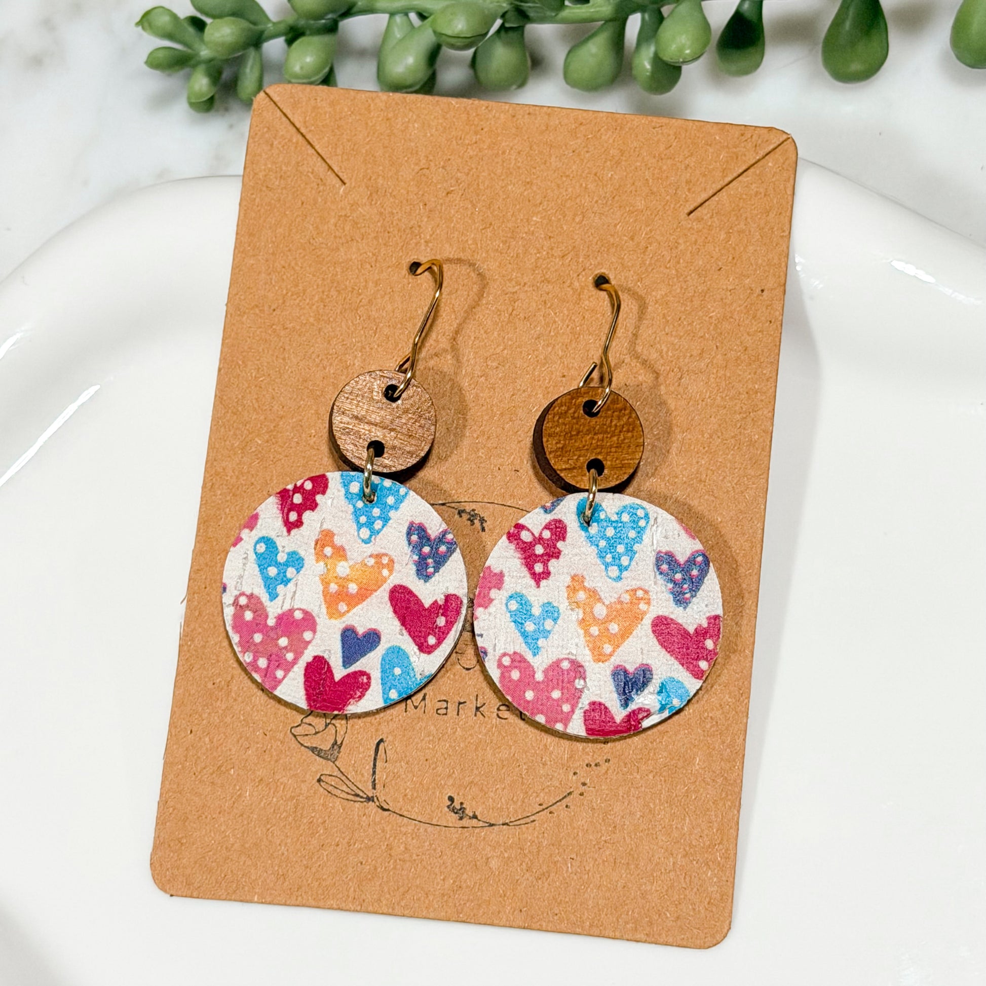 Colorful heart-patterned earrings on a brown card with green leaves in the background