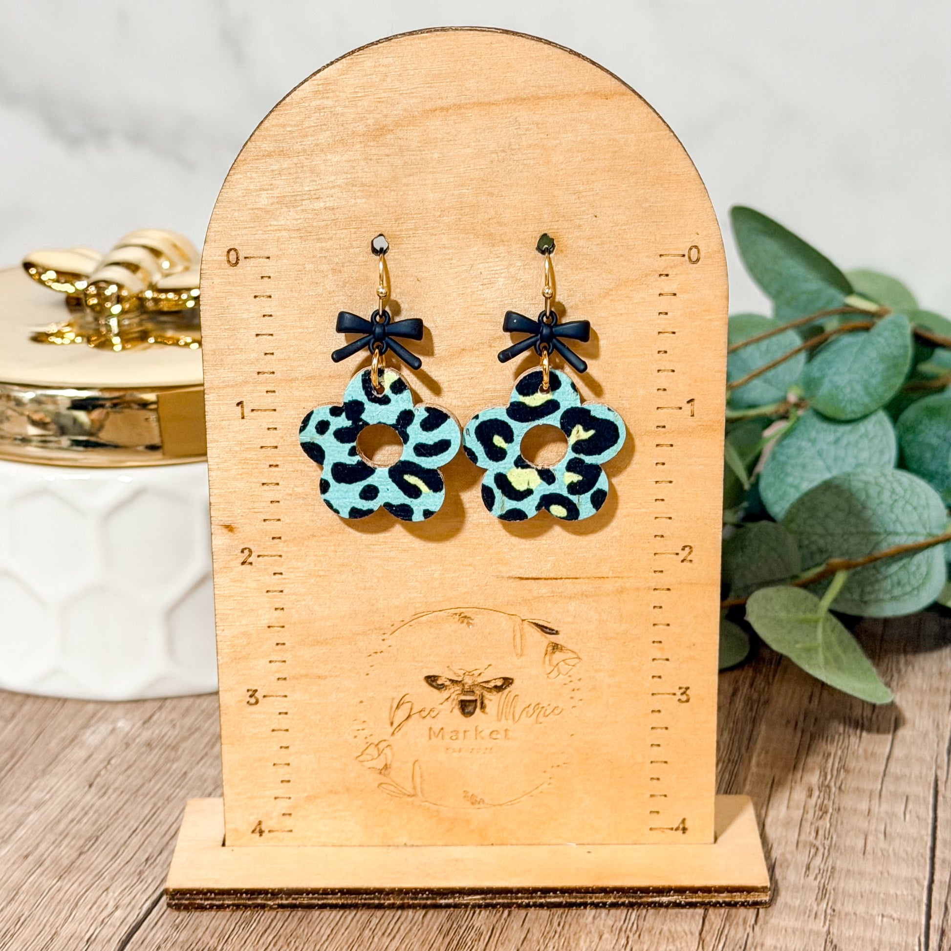 Pair of earrings with leopard print design on a wooden stand with measurement scale.