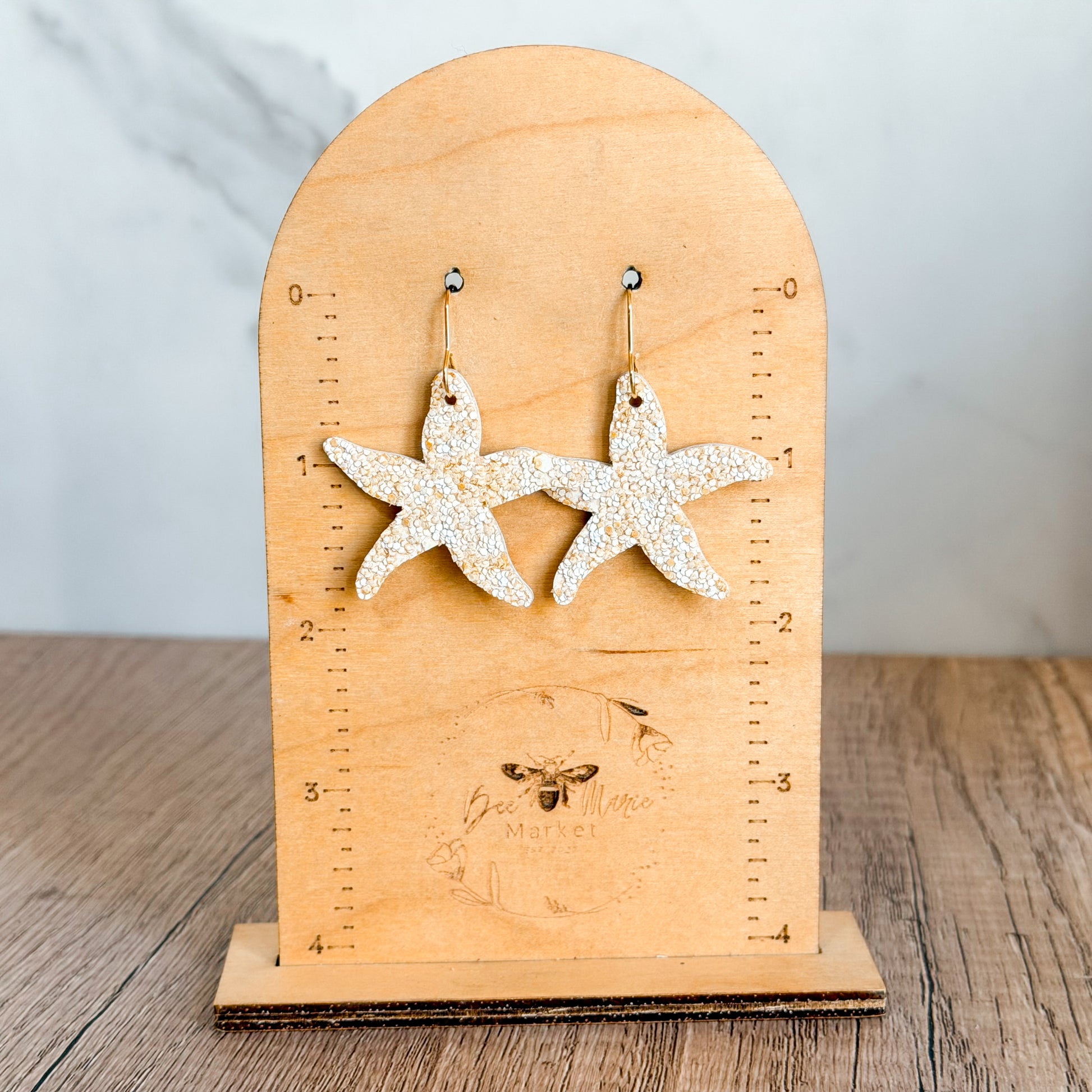 Lightweight handmade starfish earrings with textured neutral finish and gold hypoallergenic hooks displayed on wood and neutral backgrounds.