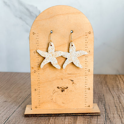 Lightweight handmade starfish earrings with textured neutral finish and gold hypoallergenic hooks displayed on wood and neutral backgrounds.