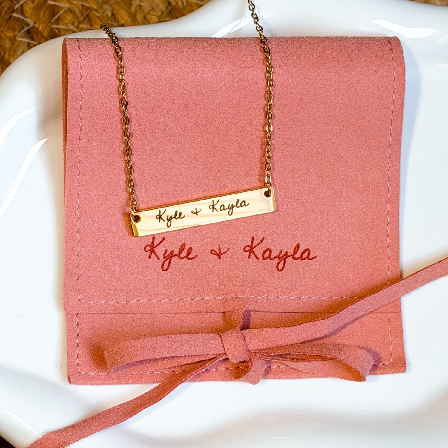 Pink wallet with a gold chain and 'Kyle & Kayla' engraving on a white surface.