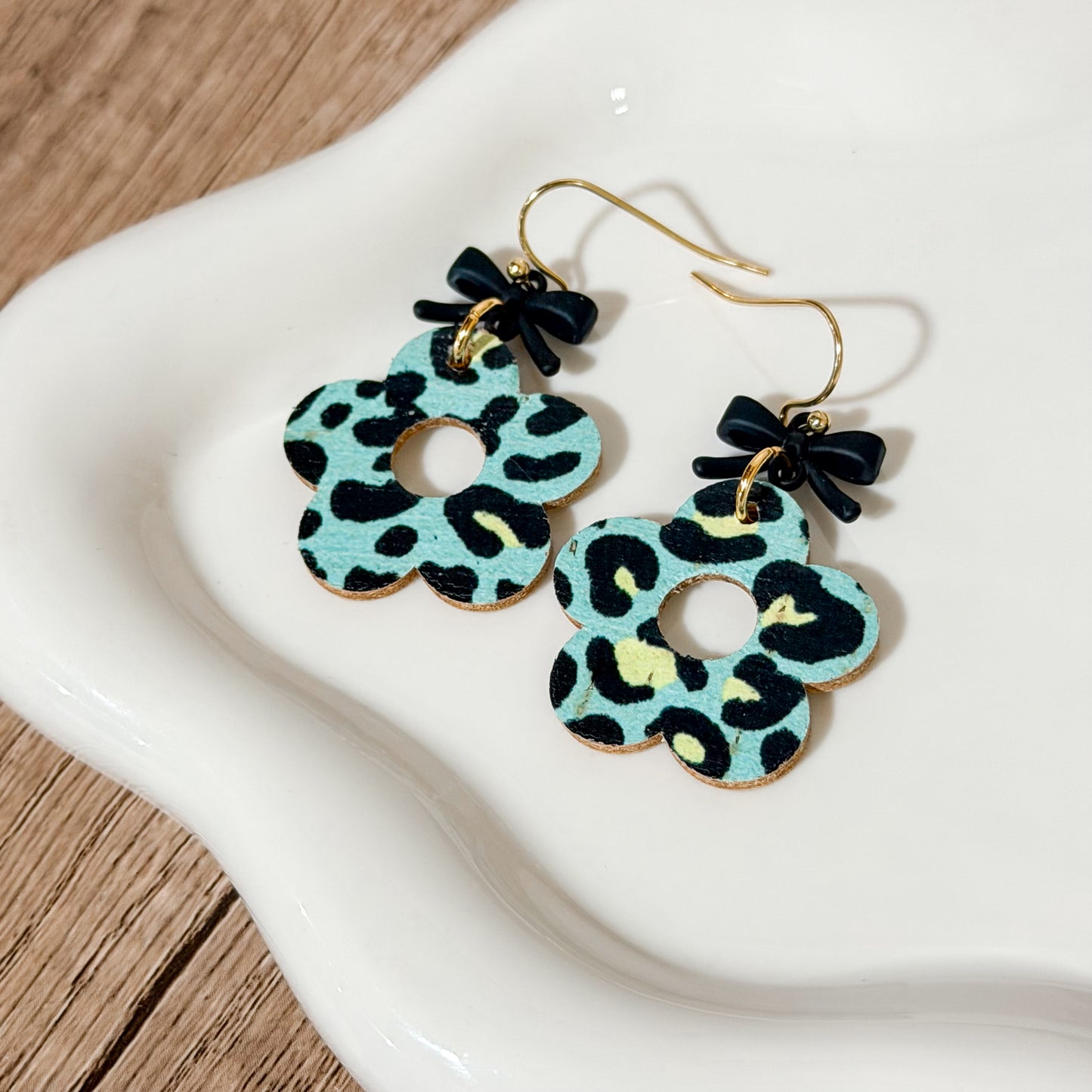 Mint leopard flower earrings with small black bow toppers displayed On white dish.