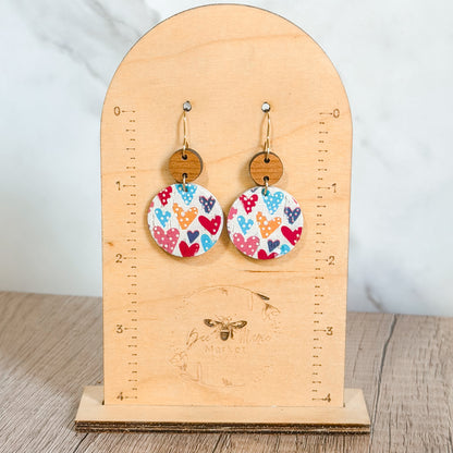 Colorful heart-patterned earrings on a wooden stand with measurement scale.