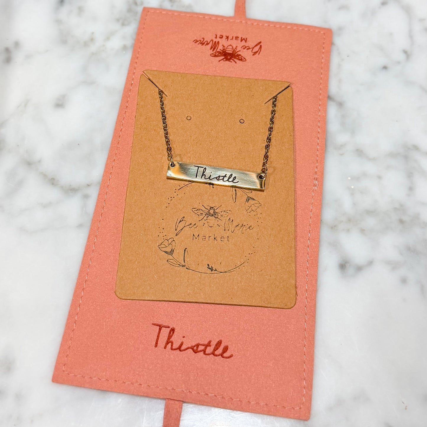 Necklace on a branded card with 'Thistle' text on a marble surface