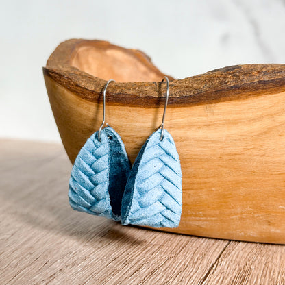 Blue chevron-patterned earrings on a wooden surface with a wooden bowl in the background.