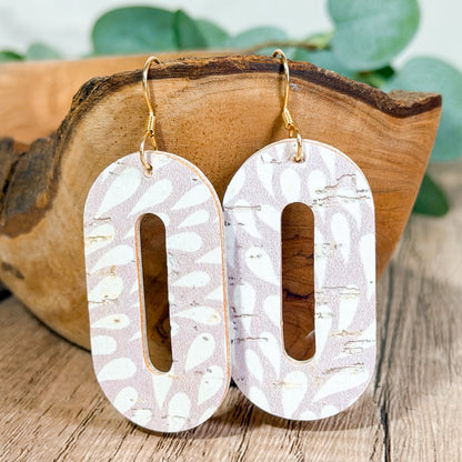 Light lavender distressed petal print leather cutout earrings with gold hooks displayed on a wooden bowl.