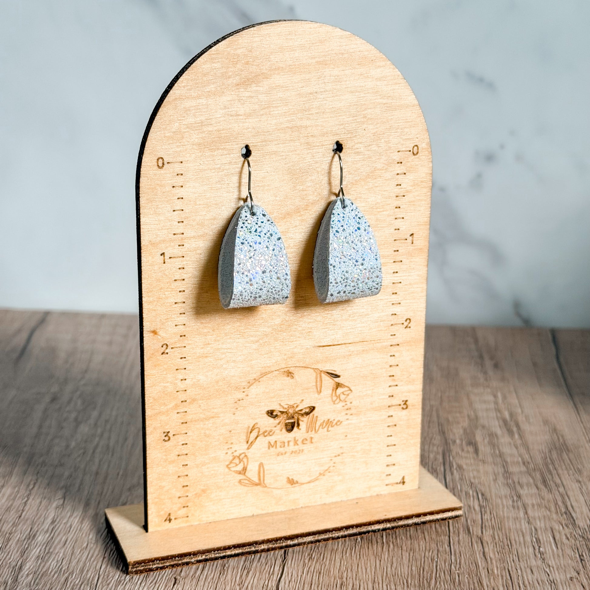 Speckled blue earrings on a wooden stand with a brand logo.