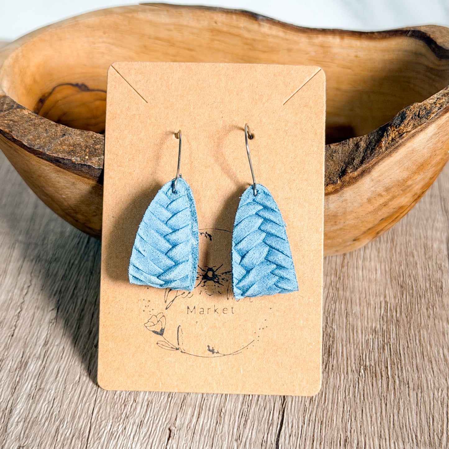 Blue chevron-patterned earrings on a brown card with a wooden bowl in the background