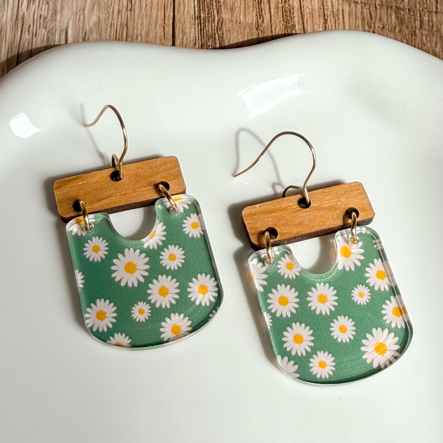 Floral patterned earrings with wooden accents on a white dish.