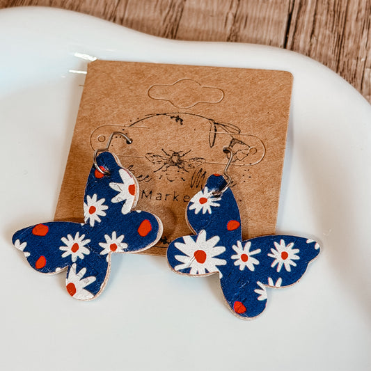 Handmade blue butterfly earrings with white daisy floral print and red accents displayed on a craft jewelry card. Lightweight patriotic summer earrings with stainless steel hooks.