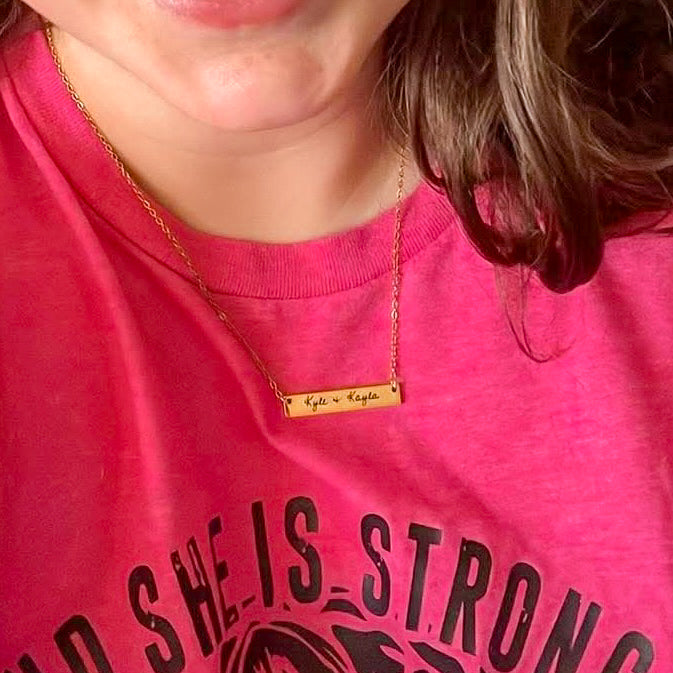 Person wearing a pink shirt with text and a gold necklace.