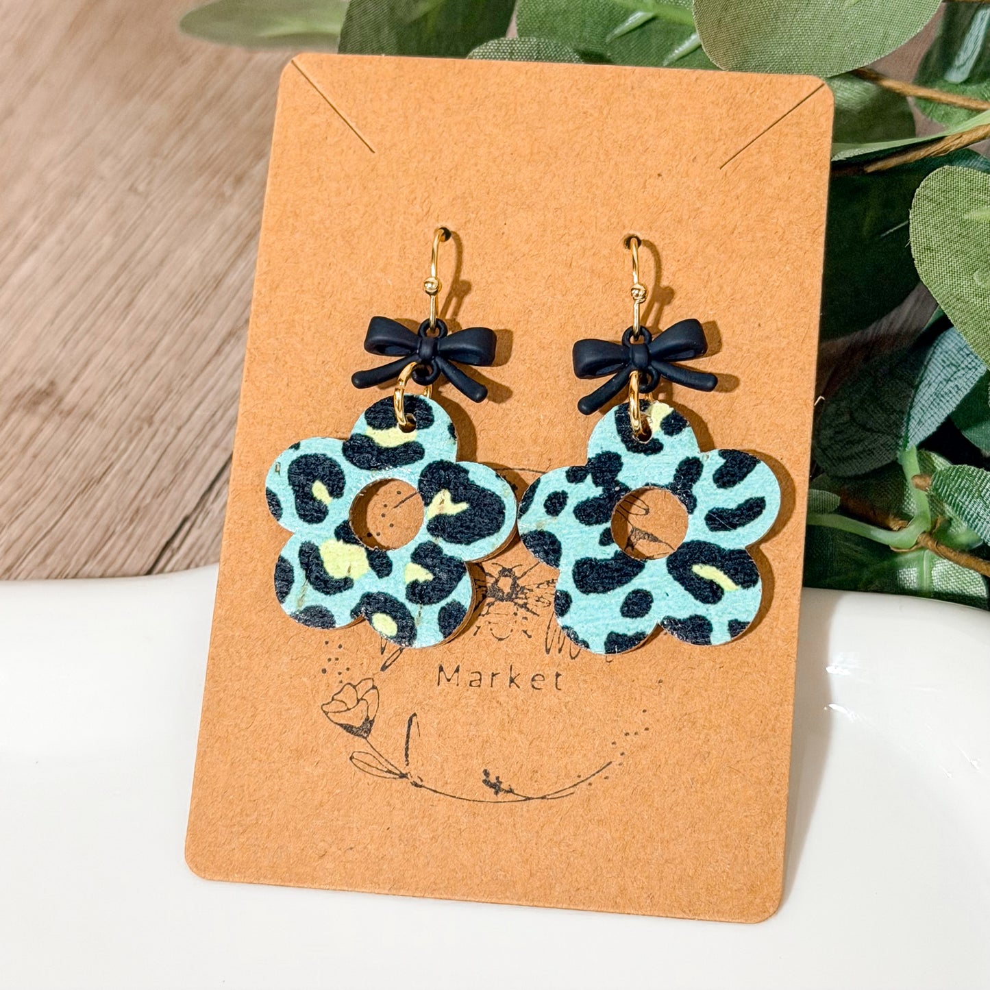 Mint leopard flower earrings with small black bow toppers displayed brown card and white jewelry dish