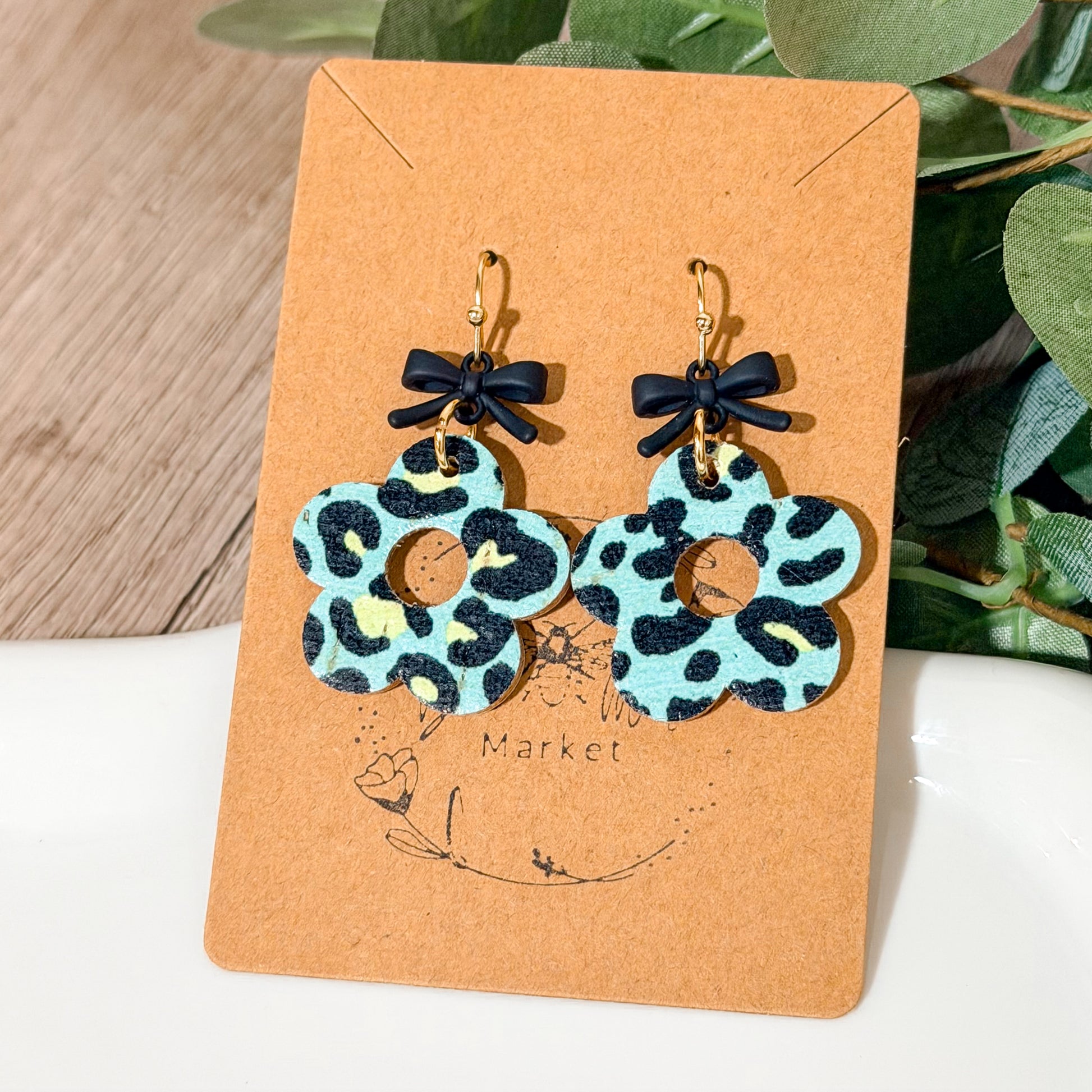 Mint leopard flower earrings with small black bow toppers displayed brown card and white jewelry dish