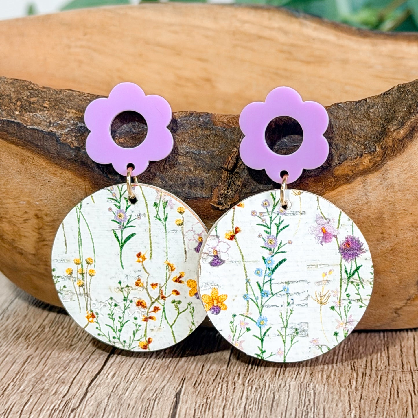 Close up of lavender flower top earrings with wildflower print circles resting on a wooden bowl.