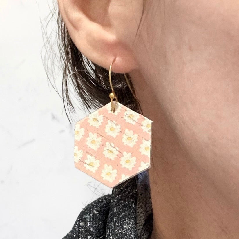 Hexagonal pink earrings with floral pattern worn by a person.