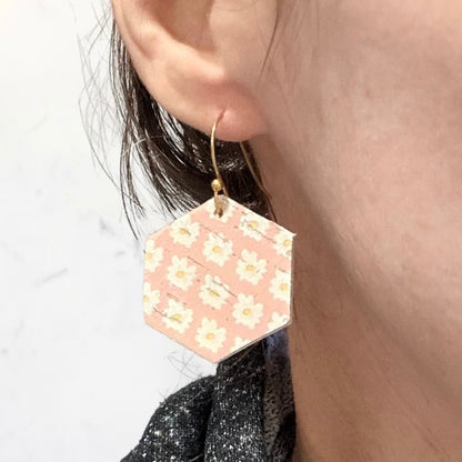 Hexagonal pink earrings with floral pattern worn by a person.