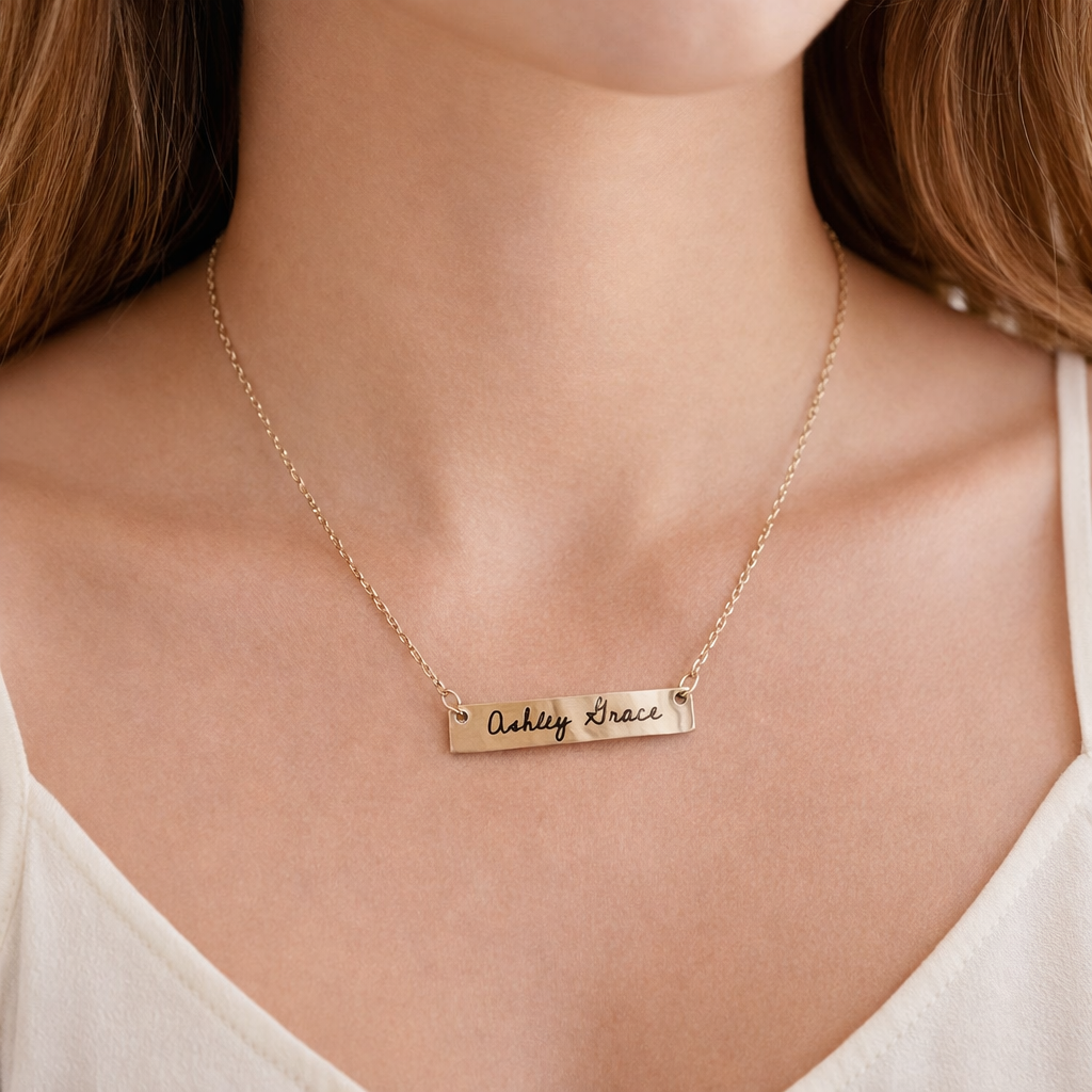 Gold necklace with engraved name on a person wearing a white top