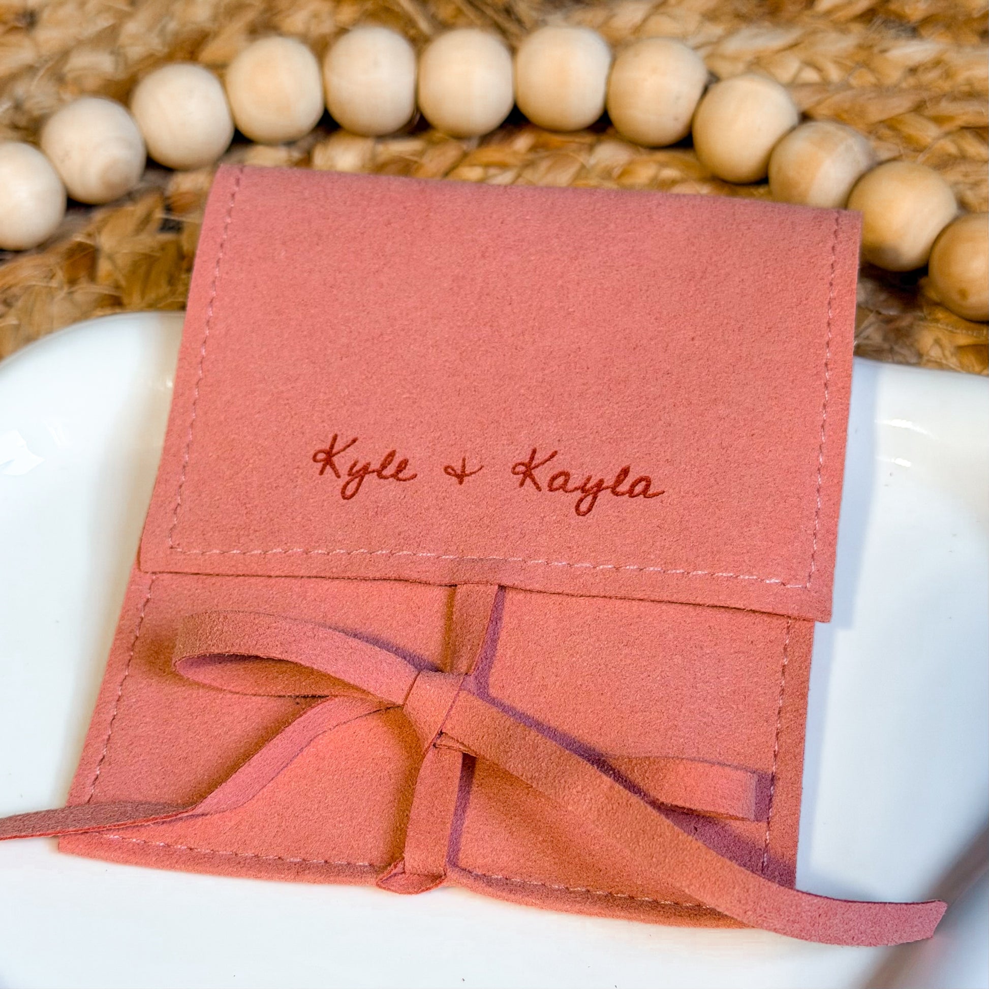 Pink fabric pouch with 'Kyle & Kayla' engraved on a woven surface.