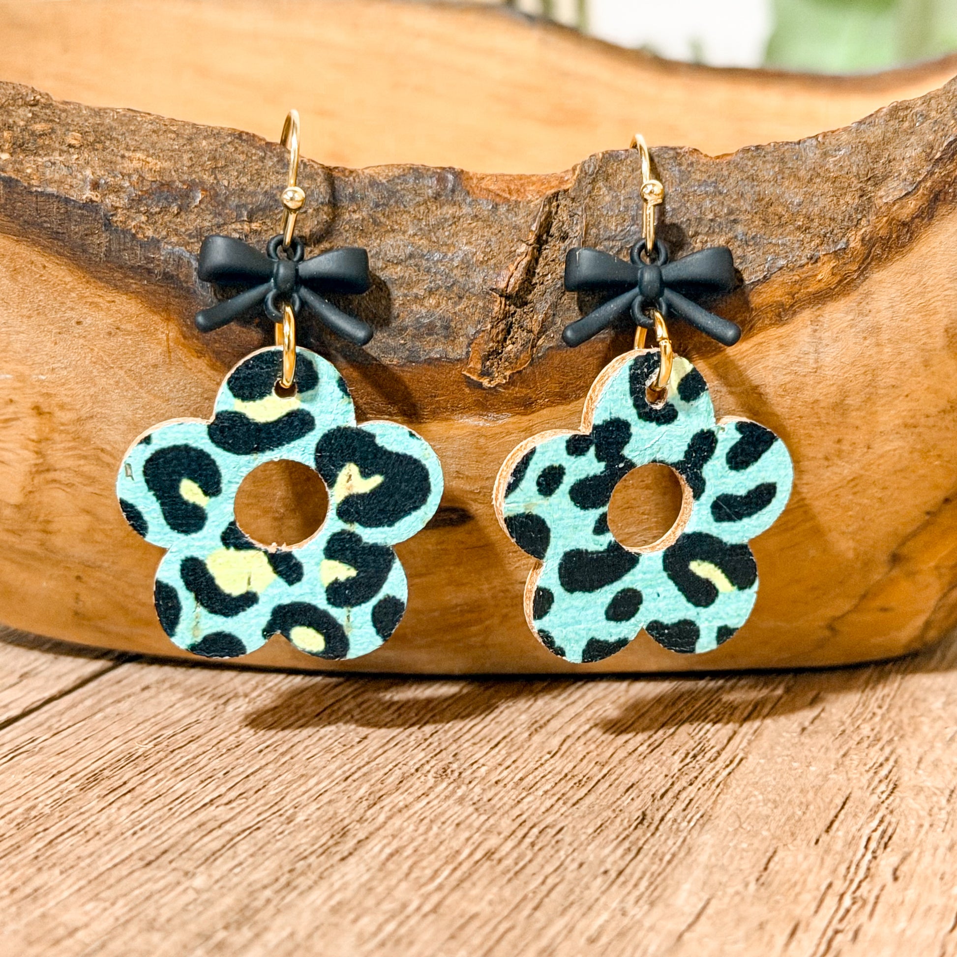 Pair of earrings with leopard print design and black bows on a wooden surface