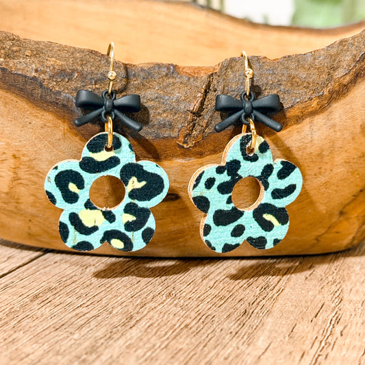 Pair of earrings with leopard print design and black bows on a wooden surface