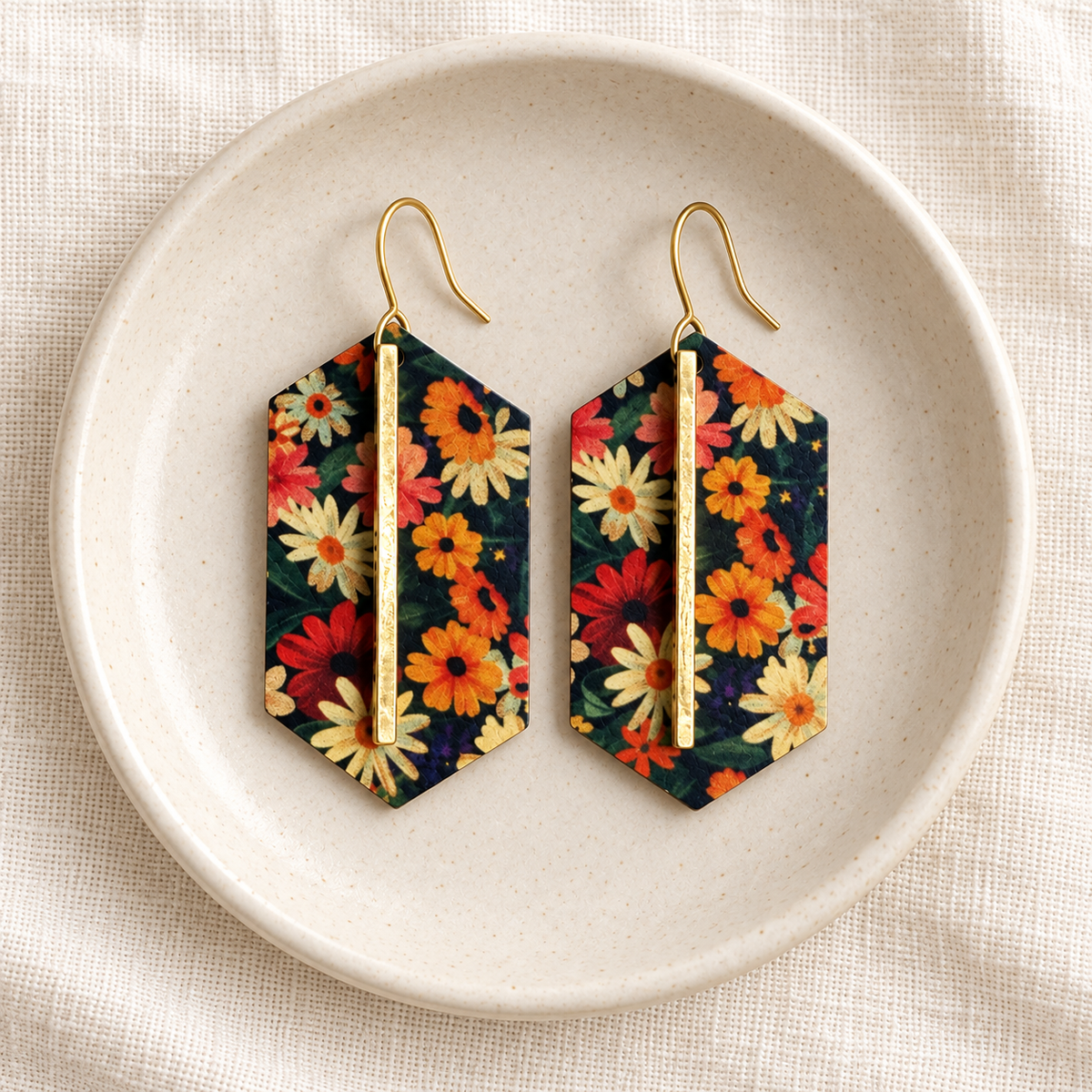 Pair of dark floral gold bar earrings in a cream jewelry dish