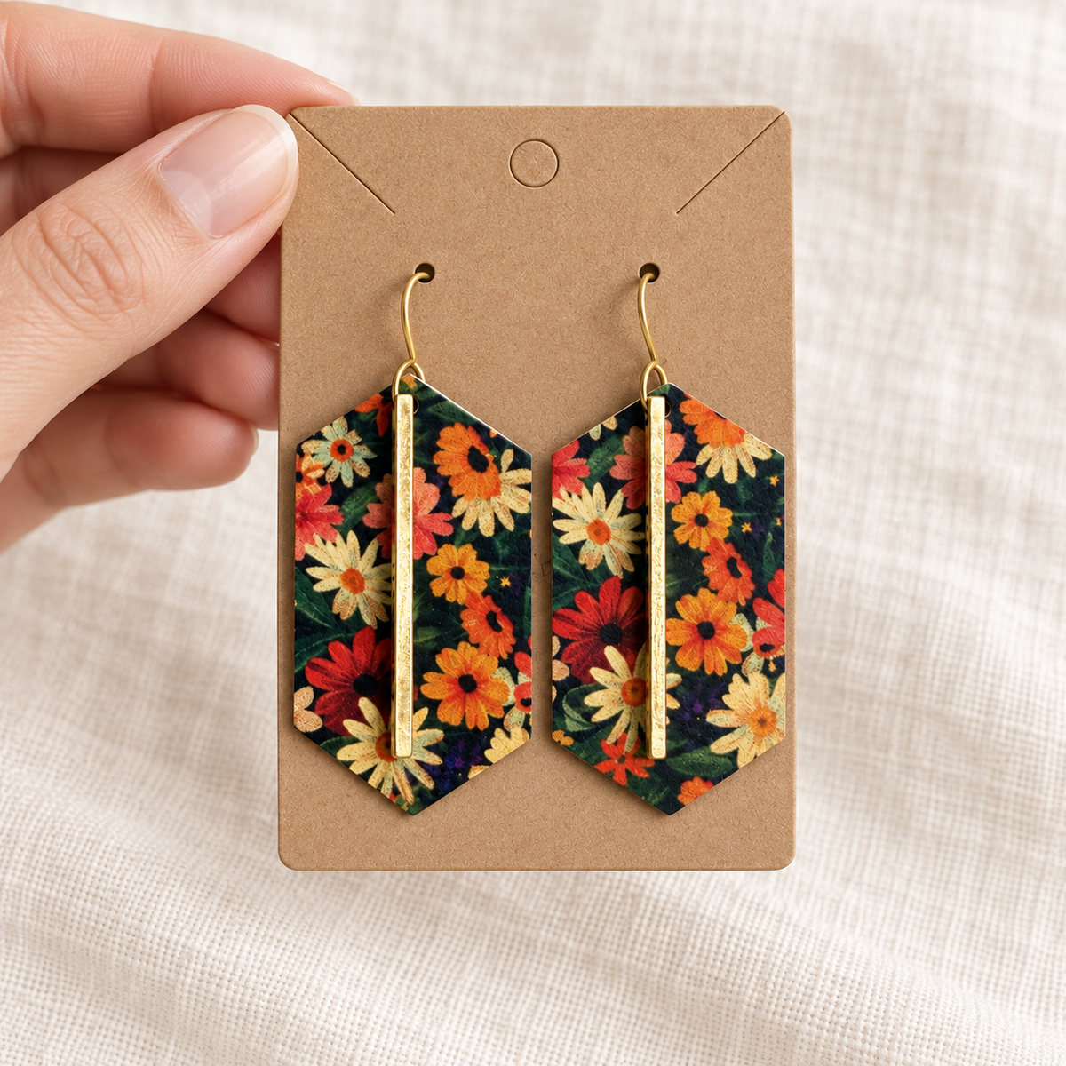Pair of dark floral gold bar earrings on a kraft card held by hand