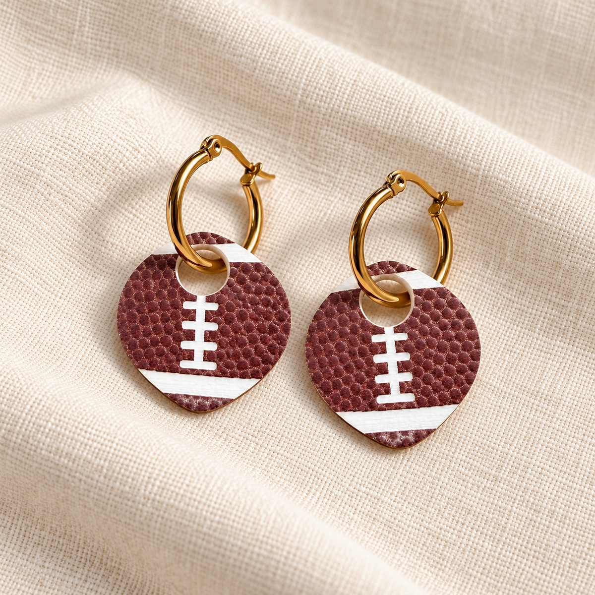 Burgundy-brown football charm hoop earrings on ivory linen