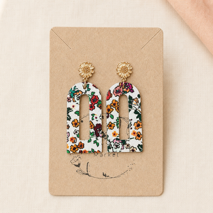 Cream floral arch earrings with gold flower studs displayed on a kraft earring card.