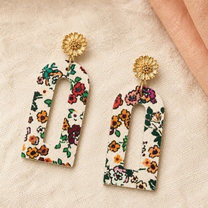 Close-up of cream floral arch earrings with textured gold flower studs.