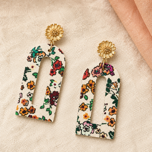 Close-up of cream floral arch earrings with textured gold flower studs.