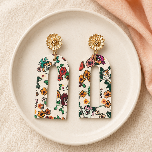 Cream floral arch earrings displayed on an ivory ceramic jewelry dish.