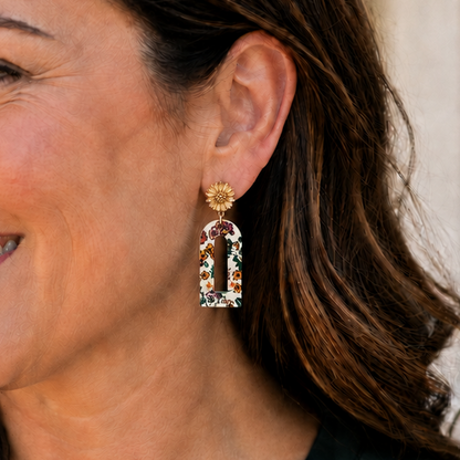 Smiling woman wearing petite cream floral arch earrings with a deep green blouse.