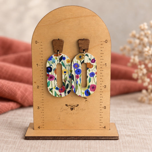 Dreamy wildflower oval open hoop earrings displayed on a wooden measuring stand.