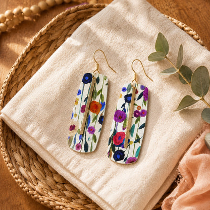 Floral bar earrings styled on ivory linen in a woven basket tray.